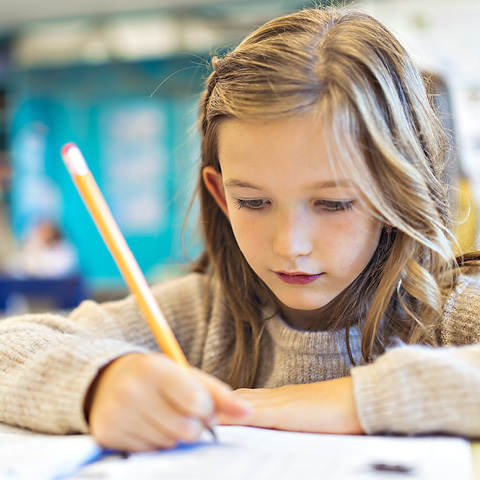 Une jeune fille en salle de classe en train d’écrire