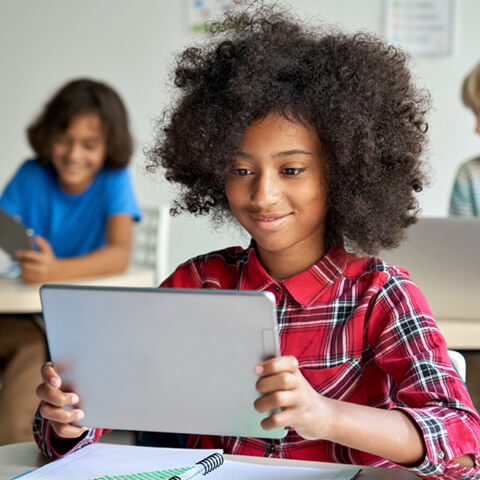 une élève tenant une tablette numérique en cours dans une salle de classe.