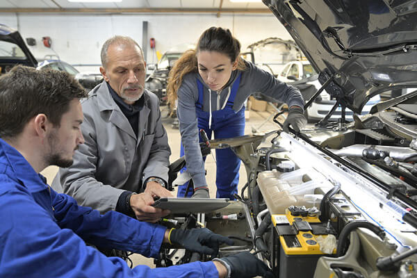un instructeur avec des élèves travaillant sur un moteur de voiture