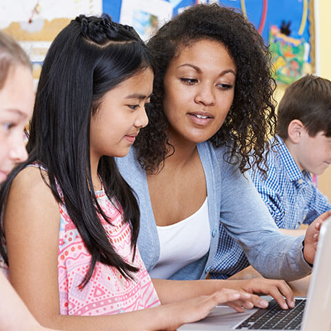 Jeune enseignante guidant une élève devant un ordinateur