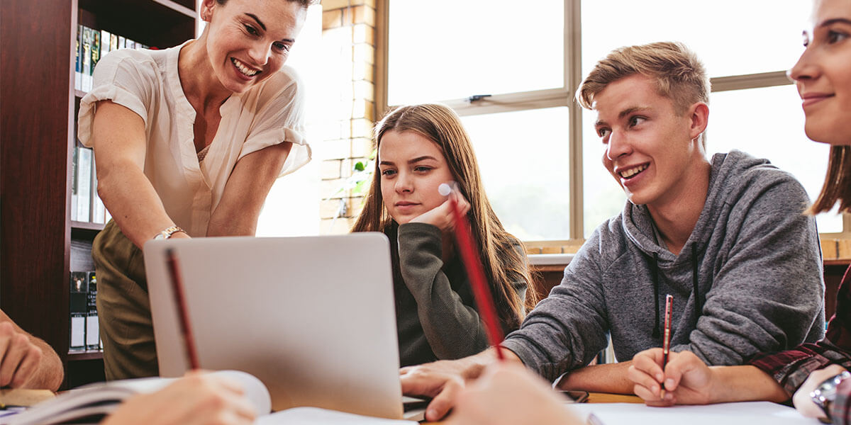 Groupe d’adolescents et enseignante pointant un ordinateur portable.