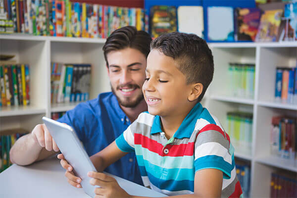 Un enseignant de maternel avec un étudiant utilisant une tablette électronique.