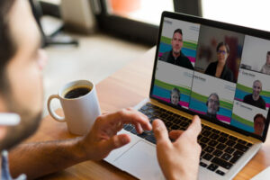 Réunion virtuelle Teams d'une équipe de spécialistes du Centre franco, en 2023. Un employé discute avec les membres de son équipe qui apparaissent sur l'écran de son laptop.