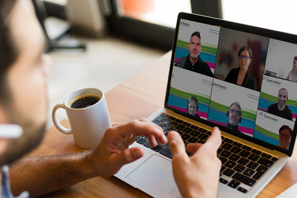 Réunion virtuelle Teams d'une équipe de spécialistes du Centre franco, en 2023. Un employé discute avec les membres de son équipe qui apparaissent sur l'écran de son laptop.